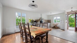 Un comedor con una mesa dispuesta para cuatro, sillas de madera, un jarrón con flores y una cocina al fondo.