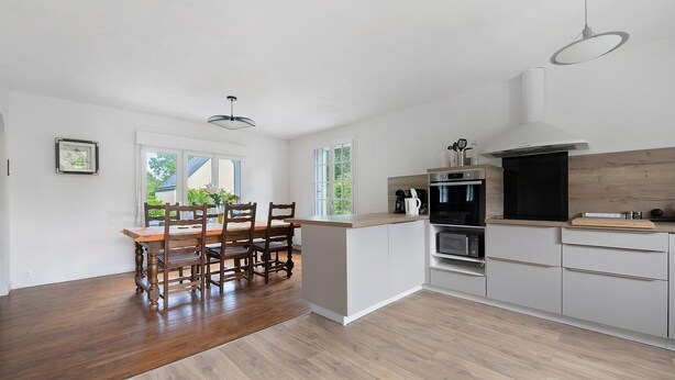 Una cocina moderna con comedor, piso de madera y ventanas amplias.