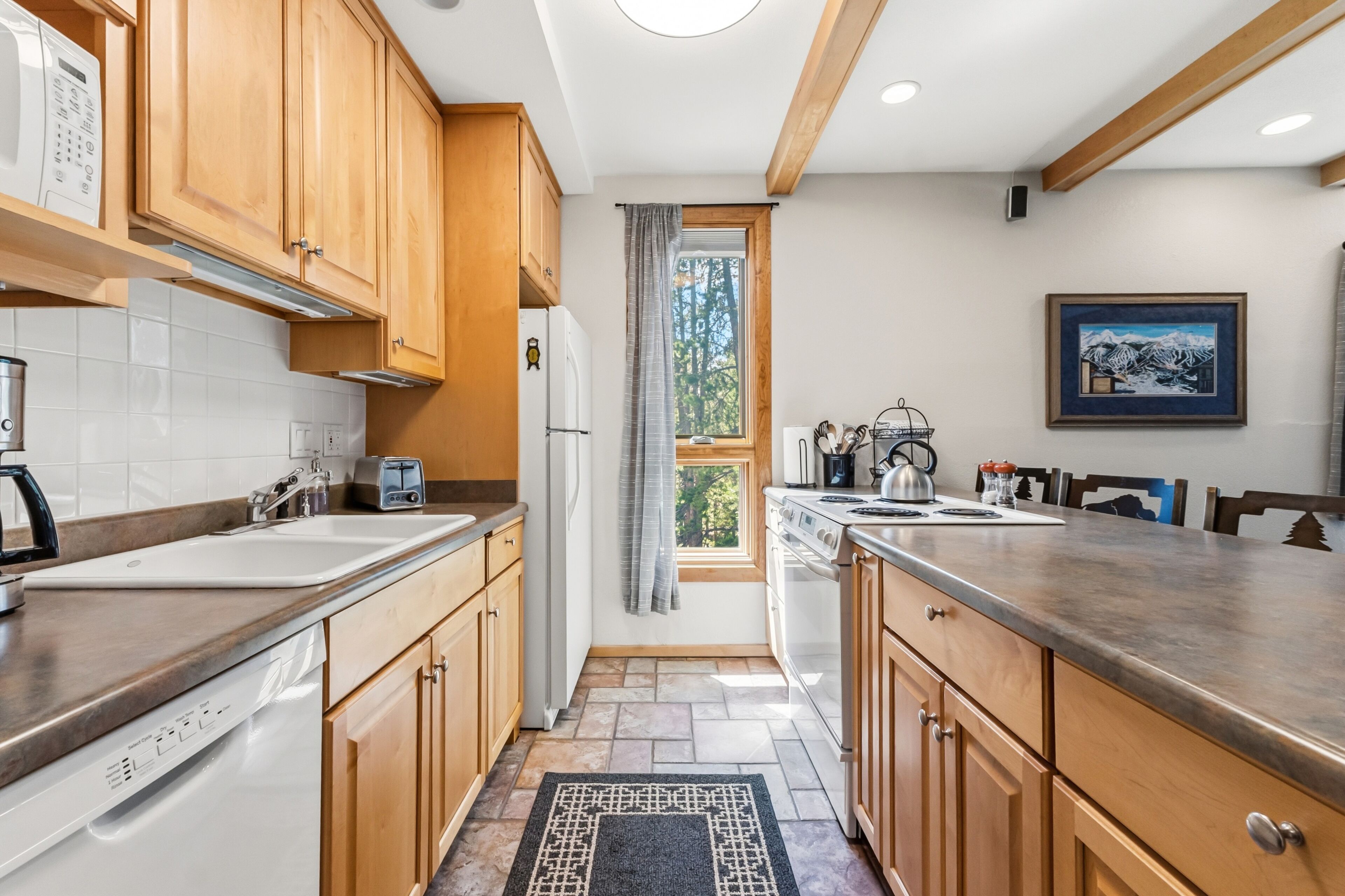 Cocina moderna con armarios de madera, lavavajillas integrado y ventana con vista a árboles.