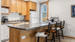 Eine Küche mit Holzausstattung, einer großen Kochinsel mit Barhocker, einem Kühlschrank und einem Fenster mit Blick auf Bäume.