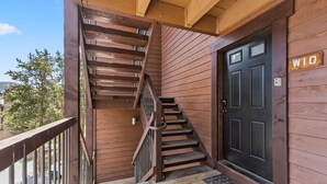 Ein Holzfassade mit einer schwarzen Tür, auf der 'W10' steht, einer Holztreppe und einem Metallgeländer.