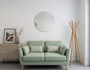 A green sofa with a round mirror above it, a wooden easel, and a framed picture on a side table. - Luxury residence near Monaco with parking and swimming pool (Beausoleil)