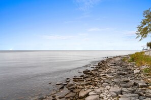 A rocky shoreline meets the calm open waters of a lake under a clear blue sky. - Owls Nest: Scenic Lakefront Retreat w/ Outdoor Fun (Sturgeon Bay)