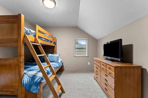 Una camera da letto con una cuccetta, un comò in legno, una televisione e una finestra.