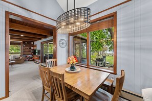 A wooden dining table and chairs sit beneath a modern cage chandelier by a scenic window. - Owls Nest: Scenic Lakefront Retreat w/ Outdoor Fun (Sturgeon Bay)