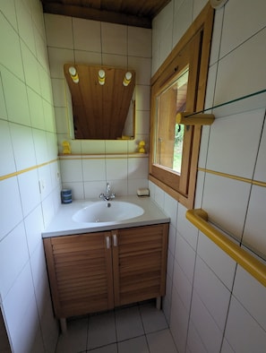 Ein Badezimmer mit einem Holzkosmetikschrank, einem weißen Waschbecken, einem Spiegel und einem Fenster.