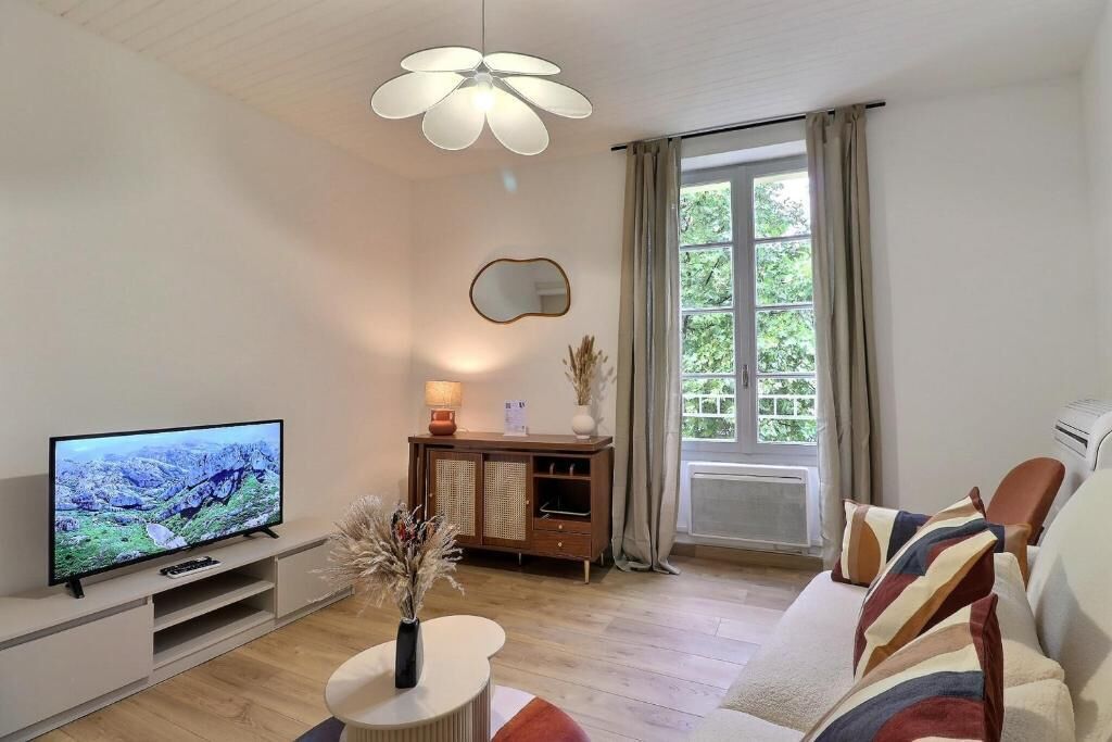 Un salon comprenant un téléviseur, un meuble, un canapé, une lampe et une fenêtre avec des rideaux.