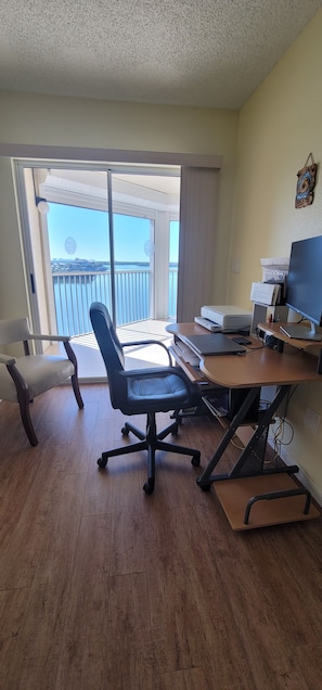 Ein Zimmer mit Schreibtisch, Stuhl, Computer und Meerblick durch eine Schiebetür.