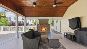 An outdoor patio with a fireplace, ceiling fans, and seating. - Sol and Sea Beach Compound w Pool and Boat House (Murrells Inlet)