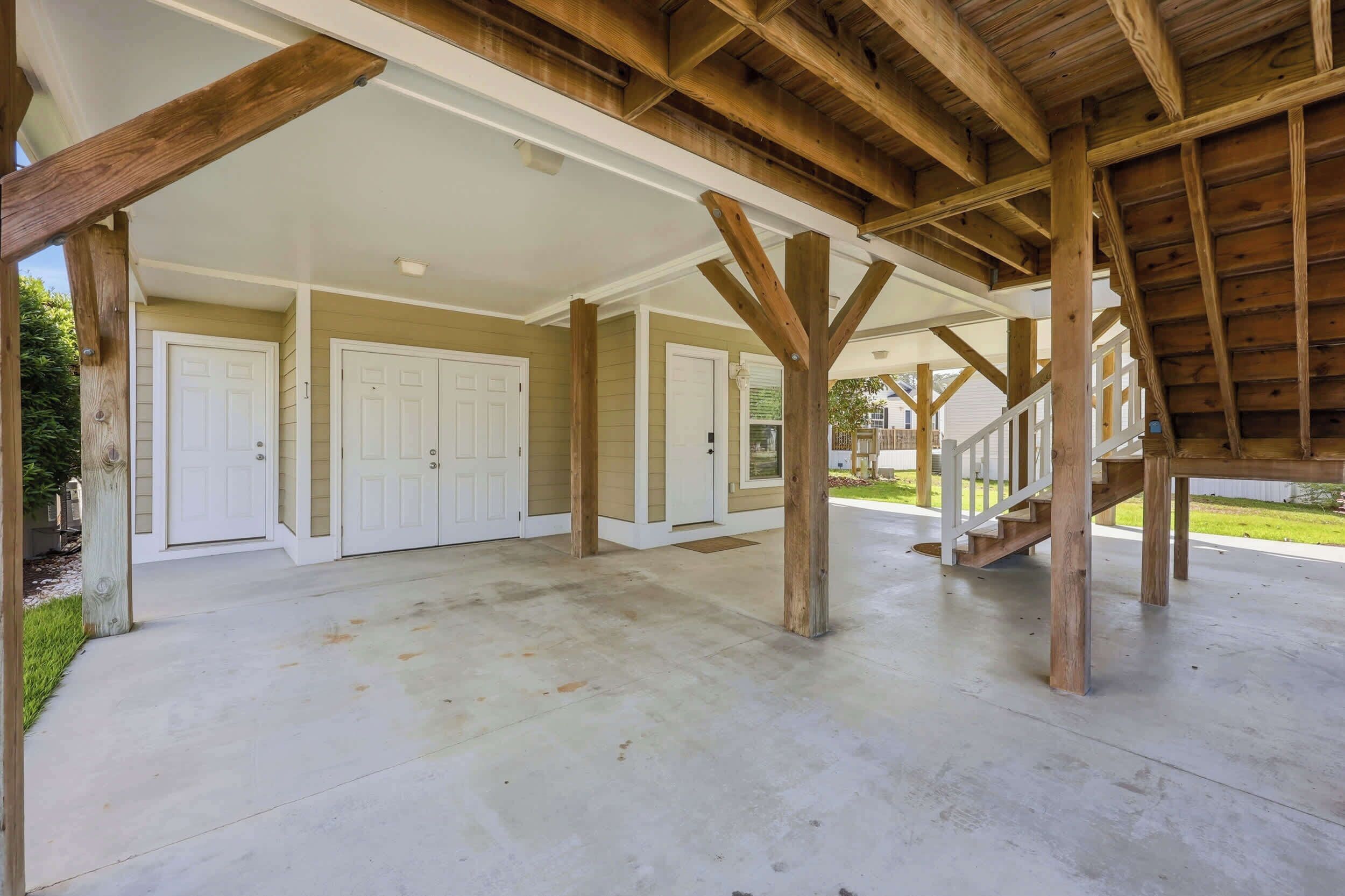 A covered outdoor area with a concrete floor, wooden beams, and white doors.