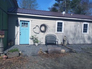 A house with a blue door, a wreath, a bench, and a statue. - Peaceful Herbal Homestead Cabin Retreat in Bristol, Maine (Bristol)