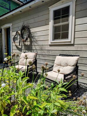 A house with two wicker chairs with cushions, a wreath on the wall, and a window. - Peaceful Herbal Homestead Cabin Retreat in Bristol, Maine (Bristol)