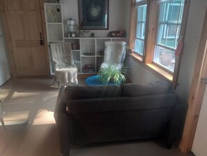 Ett vardagsrum med en mörk soffa, två vita stolar, ett blått bord och en krukväxt.