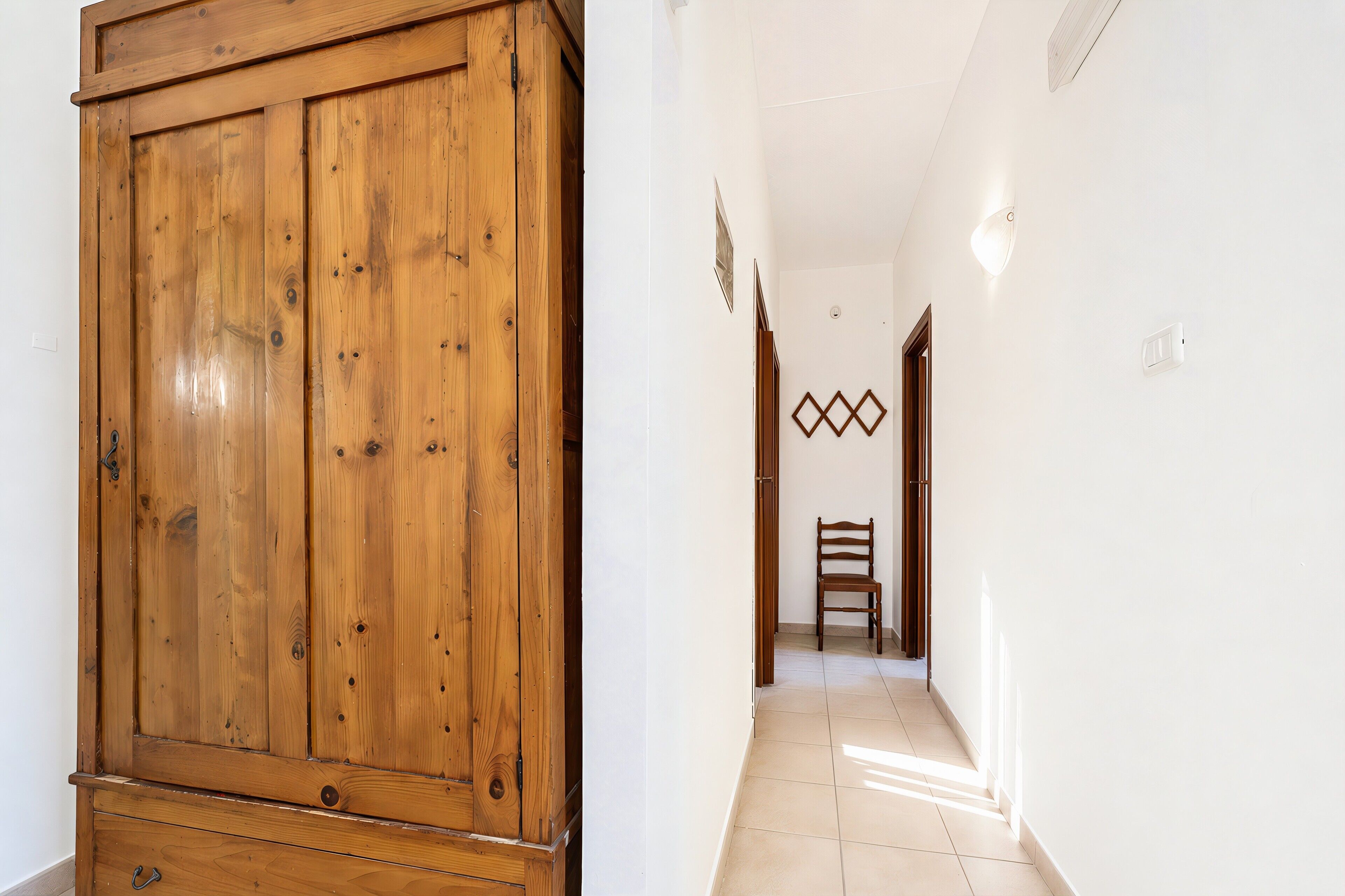 A hallway with a wooden wardrobe, a chair, and a wall-mounted light fixture.
