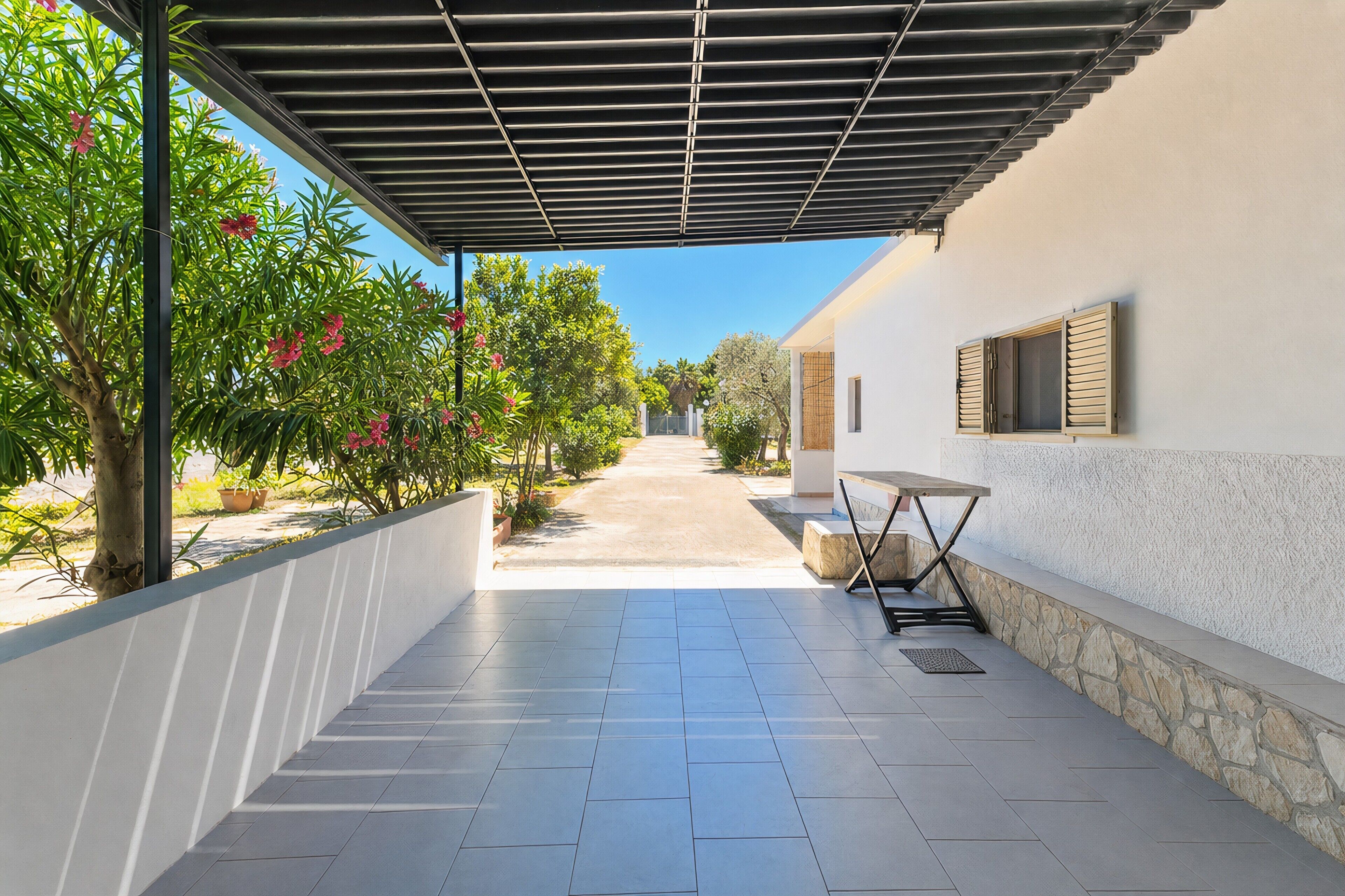 A covered outdoor area with a tiled floor, a table, and a bench.