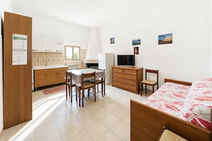 Ein Zimmer mit einem Bett, einem Fernseher, einem Esstisch mit Stühlen, einer Küchenzeile und einem Holzschrank.