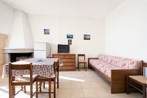 Ein Zimmer mit Esstisch, Stühlen, einer Couch, einem Fernseher und einem Kamin.