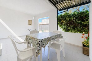 Ein Essbereich mit Tisch und Stühlen, ein Fenster mit Blick auf Gebäude und eine Wand mit Grünpflanzen.