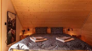 A cozy room with a wooden ceiling, a bed with a patterned bedspread, two pillows, and a painting on the wall.