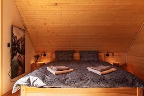 Una habitación acogedora con techo de madera, una cama con colcha estampada, dos almohadas y un cuadro en la pared.