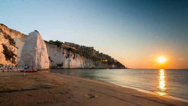 Ein Strand mit weißen Klippen, einem Sonnenuntergang und ruhiger See.