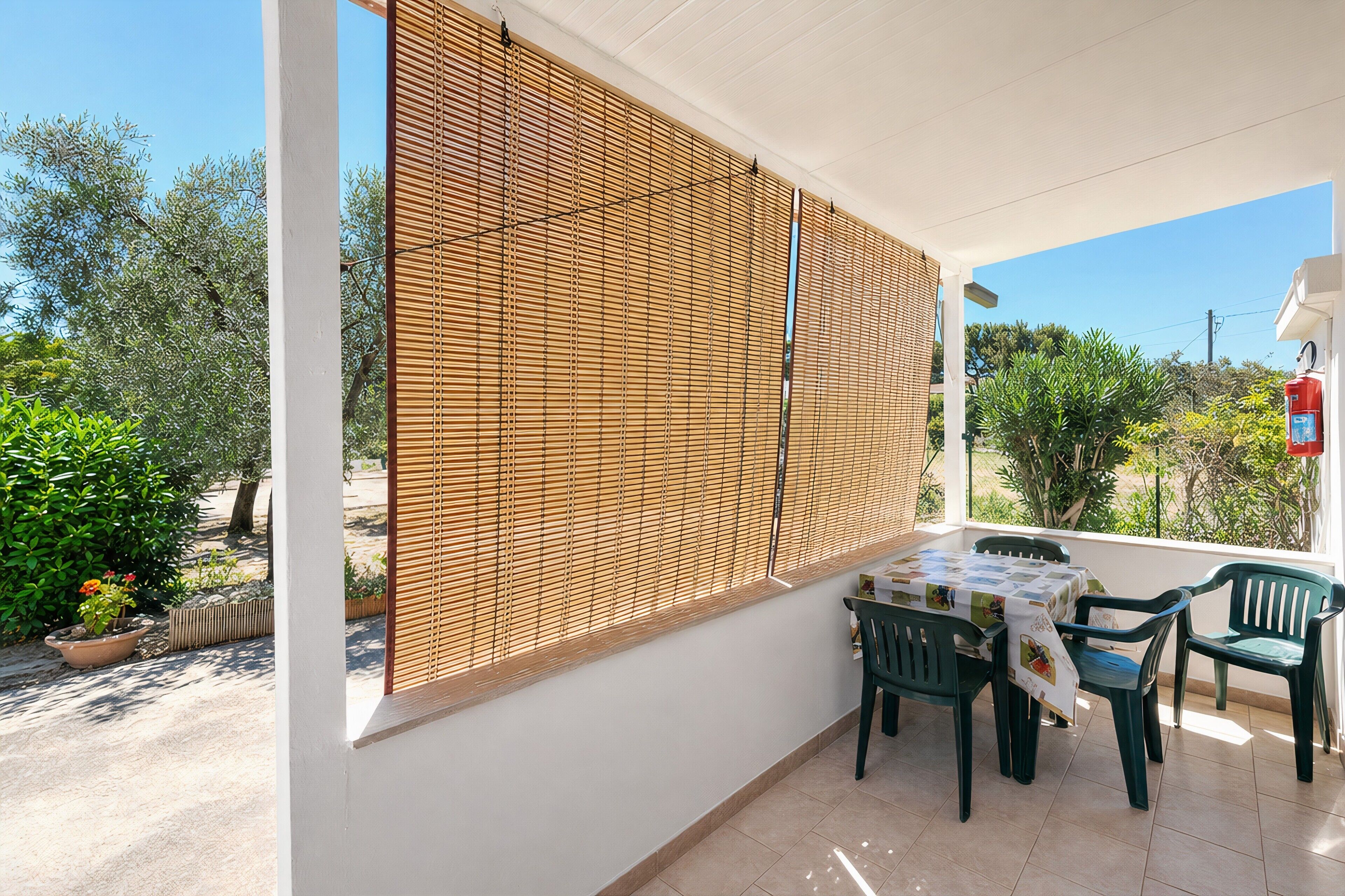 A covered patio with a table and chairs, a wooden blind, and a fire extinguisher.