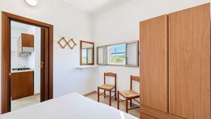 Ein Schlafzimmer mit Bett, Holzschrank, zwei Stühlen, einem kleinen Tisch und einem Fenster mit Blick.