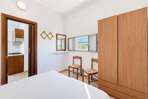 Ein Schlafzimmer mit Bett, Holzschrank, zwei Stühlen, einem kleinen Tisch und einem Fenster mit Blick.