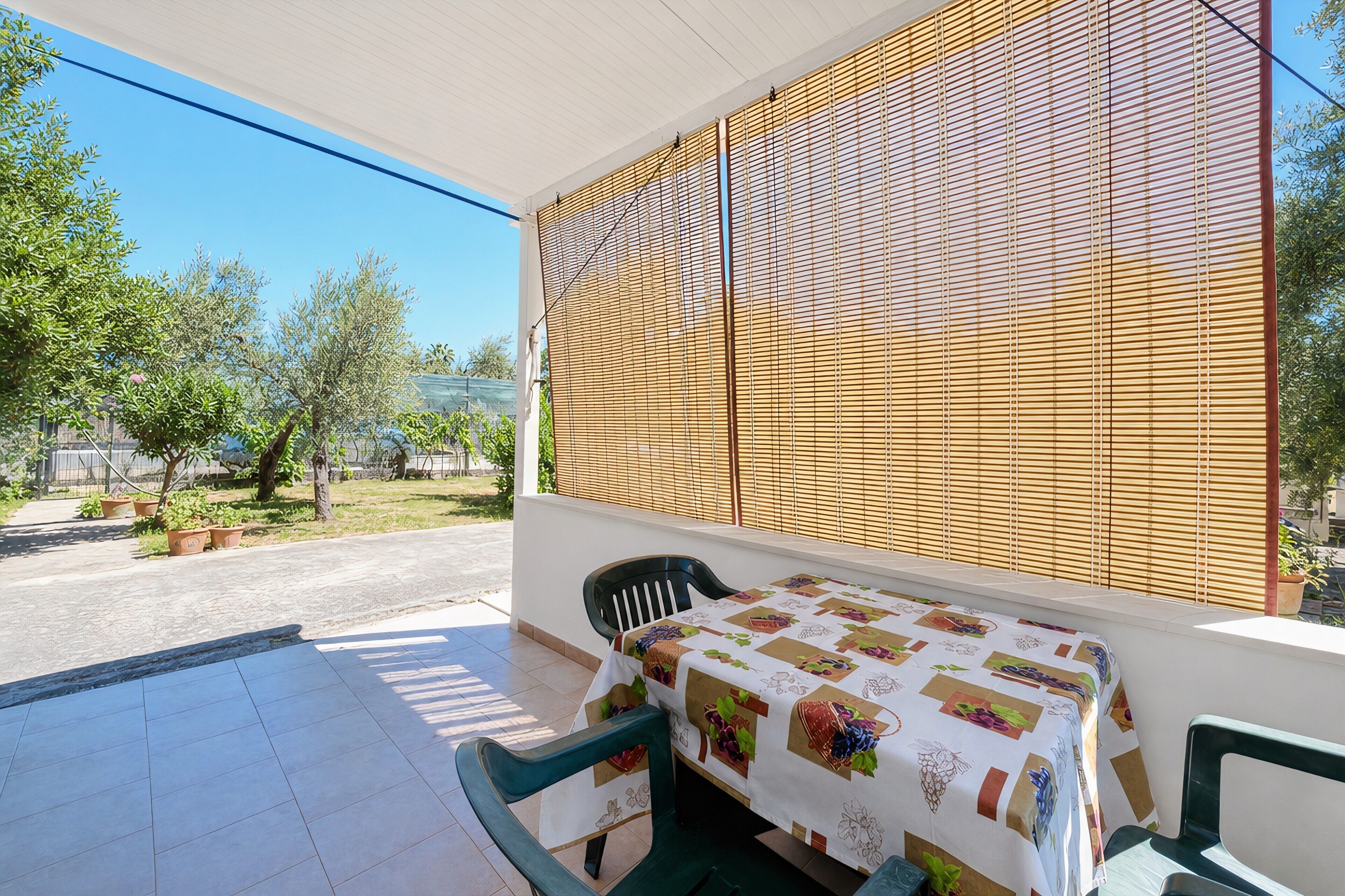 A balcony with a table and chairs, a wooden privacy screen, and a view of trees and a street.