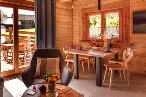 Interior acogedor de una cabaña con comedor, un sofá con cojín y ventana con vistas al exterior.