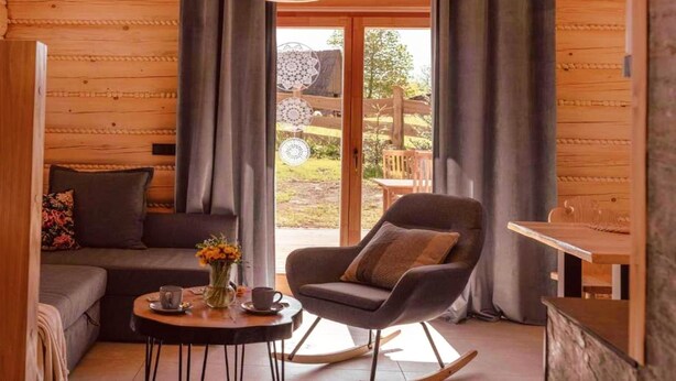 A cozy room with a sofa, a rocking chair, a small table with a cup and flowers, and a view of the outdoors.