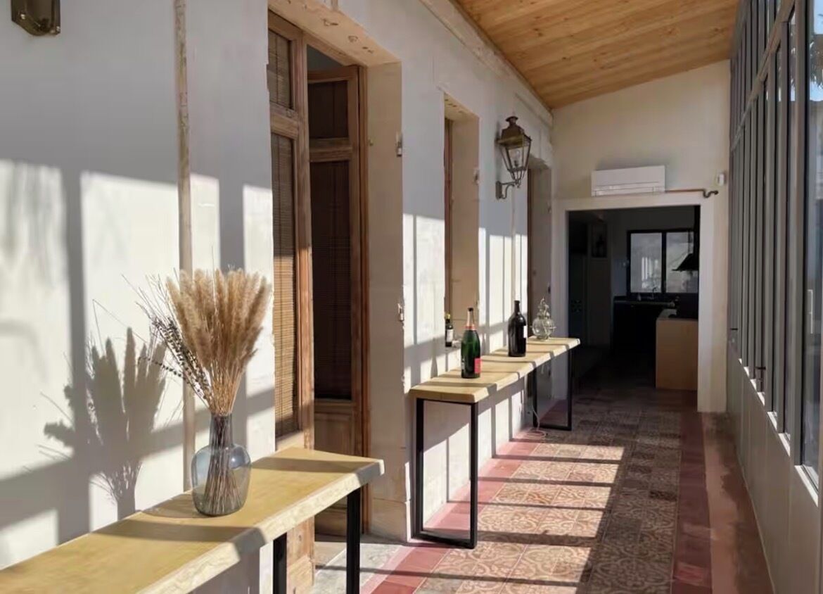 Een gang met een houten plafond, betegelde vloer en een rij tafels met flessen.