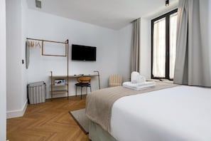 A hotel room with a bed, a desk with a chair, a television, and a window with curtains. - CSE MS MUSEO SELECT (Sevilla)