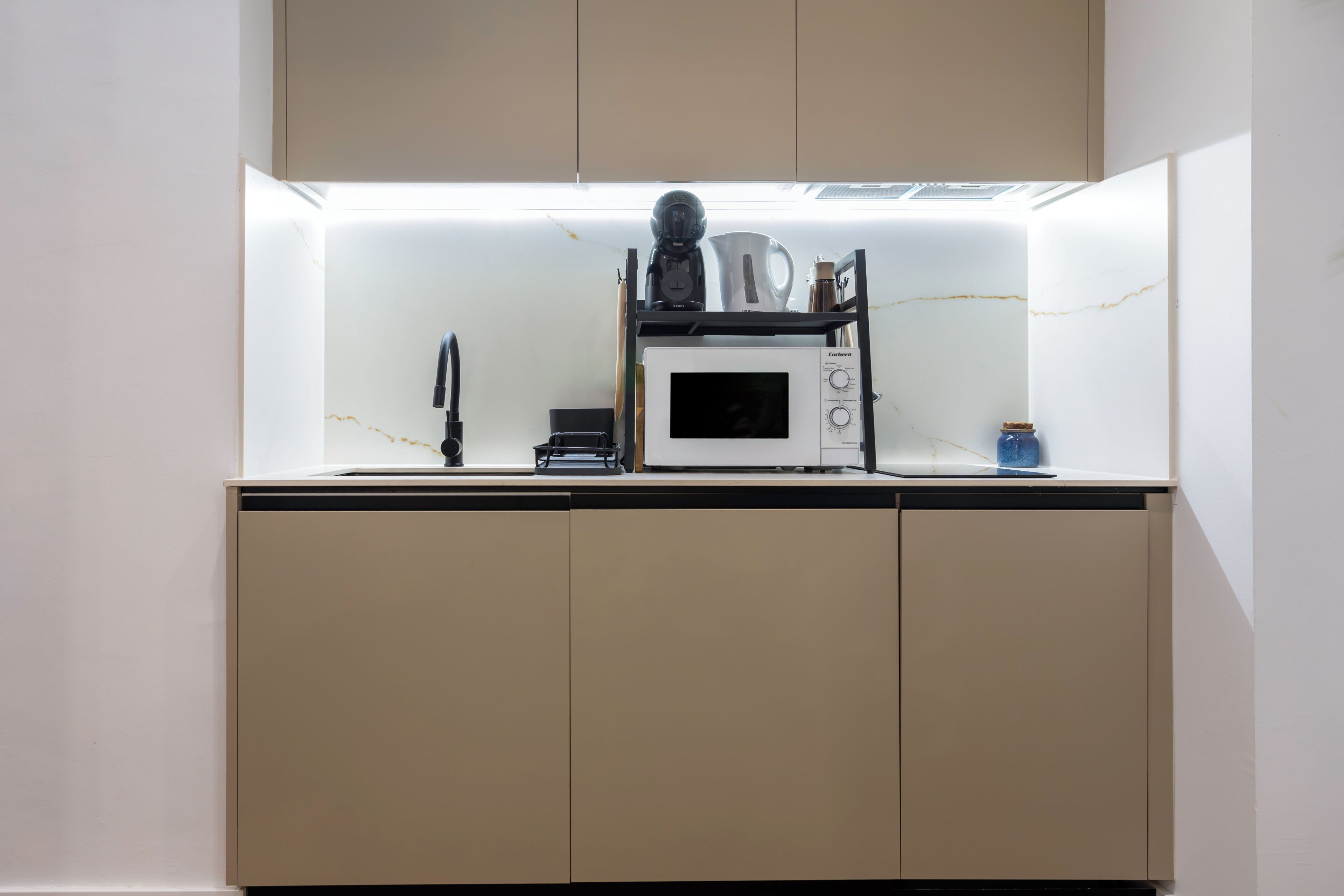 Una cocina compacta con microondas, hervidor y cafetera sobre la encimera.