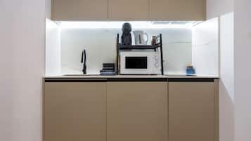 Una cocina compacta con microondas, hervidor y cafetera sobre la encimera.