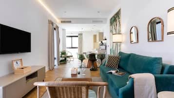 A modern living room with a flat-screen TV, a teal sofa, a dining table, and a wicker chair.