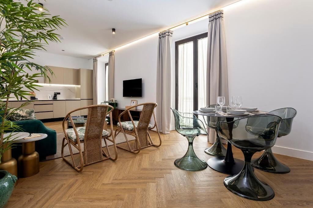 A modern living room with a dining area, including wicker chairs, a glass table, and a television.