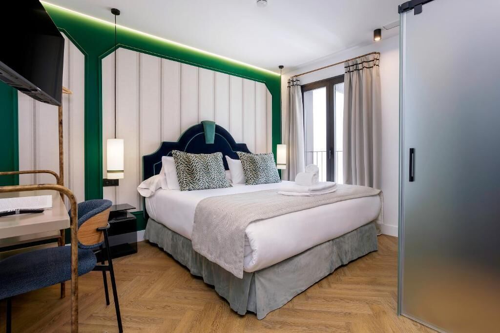 A hotel room with a bed, bedside table, chair, and a TV.
