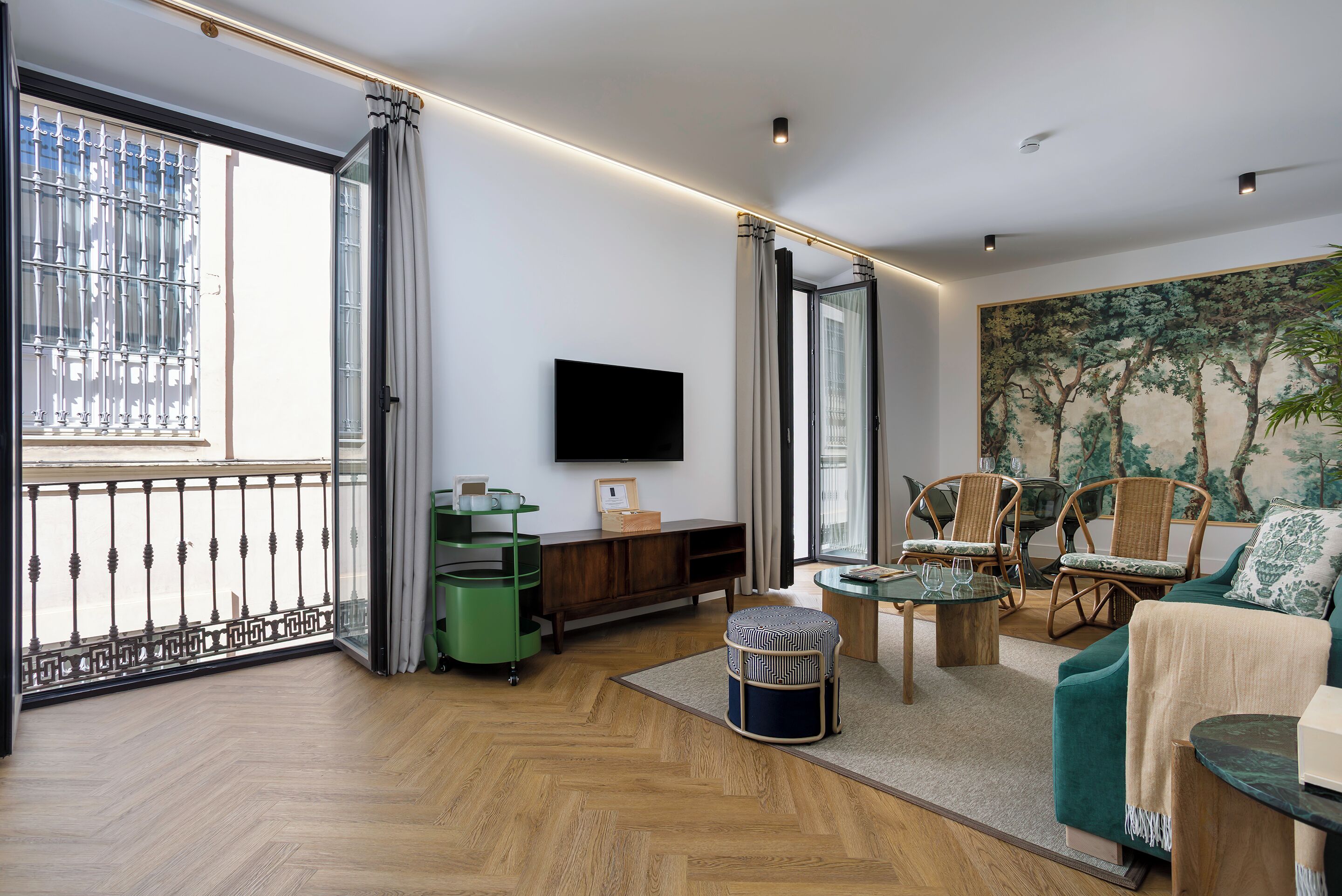 A modern living room with a large window, a flat-screen TV, wicker furniture, and a painting on the wall.