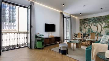 A modern living room with a large window, a flat-screen TV, wicker furniture, and a painting on the wall.