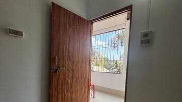 A room with a wooden door, a tiled floor, and a view through a window with a metal grid.