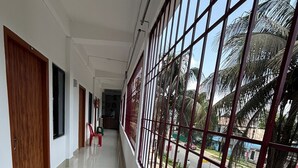 A corridor with a view of the street outside, featuring a metal railing and a wooden door on the left.