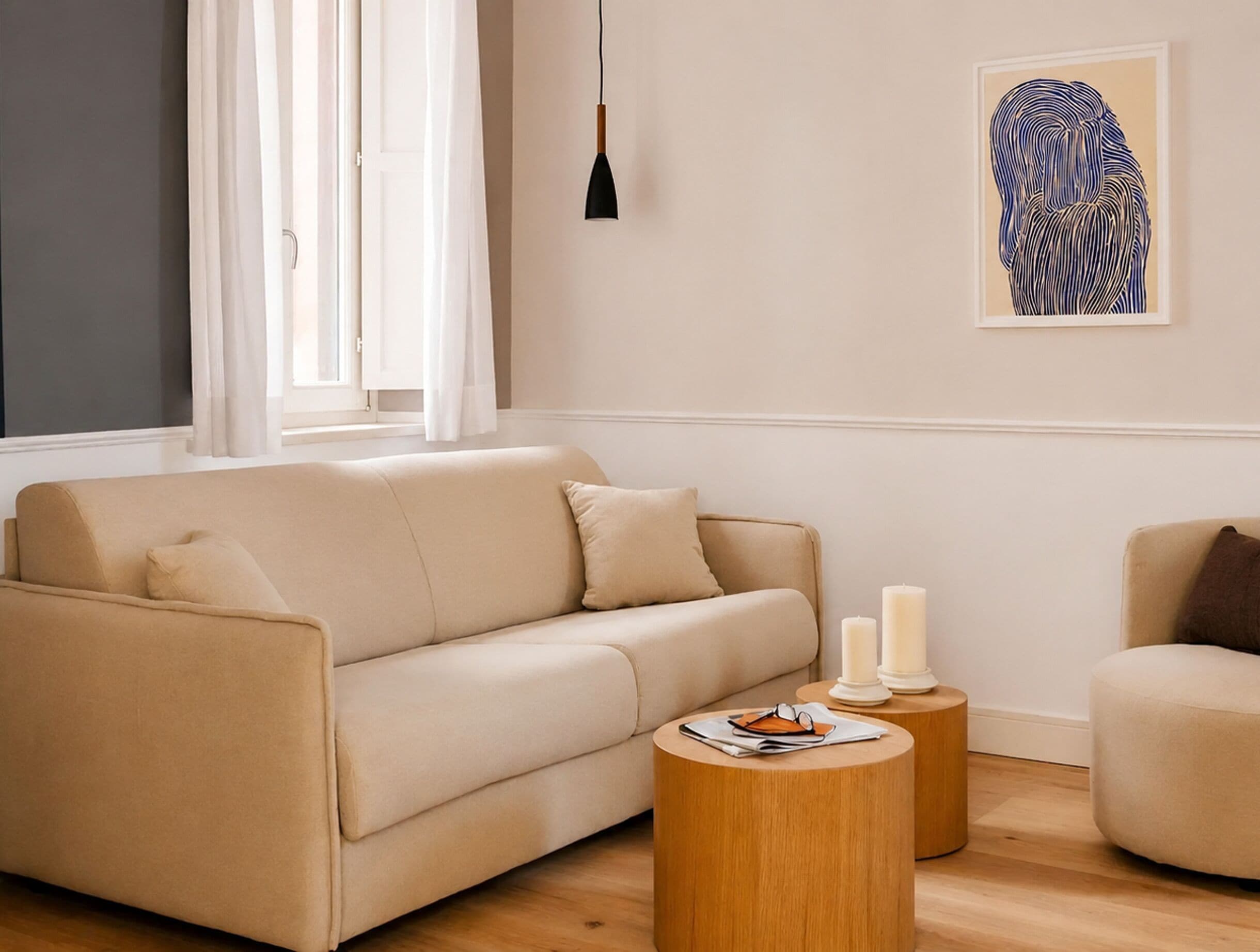 Un salón con un sofá, dos mesitas de madera redondas, una lámpara colgante y una obra de arte enmarcada en la pared.