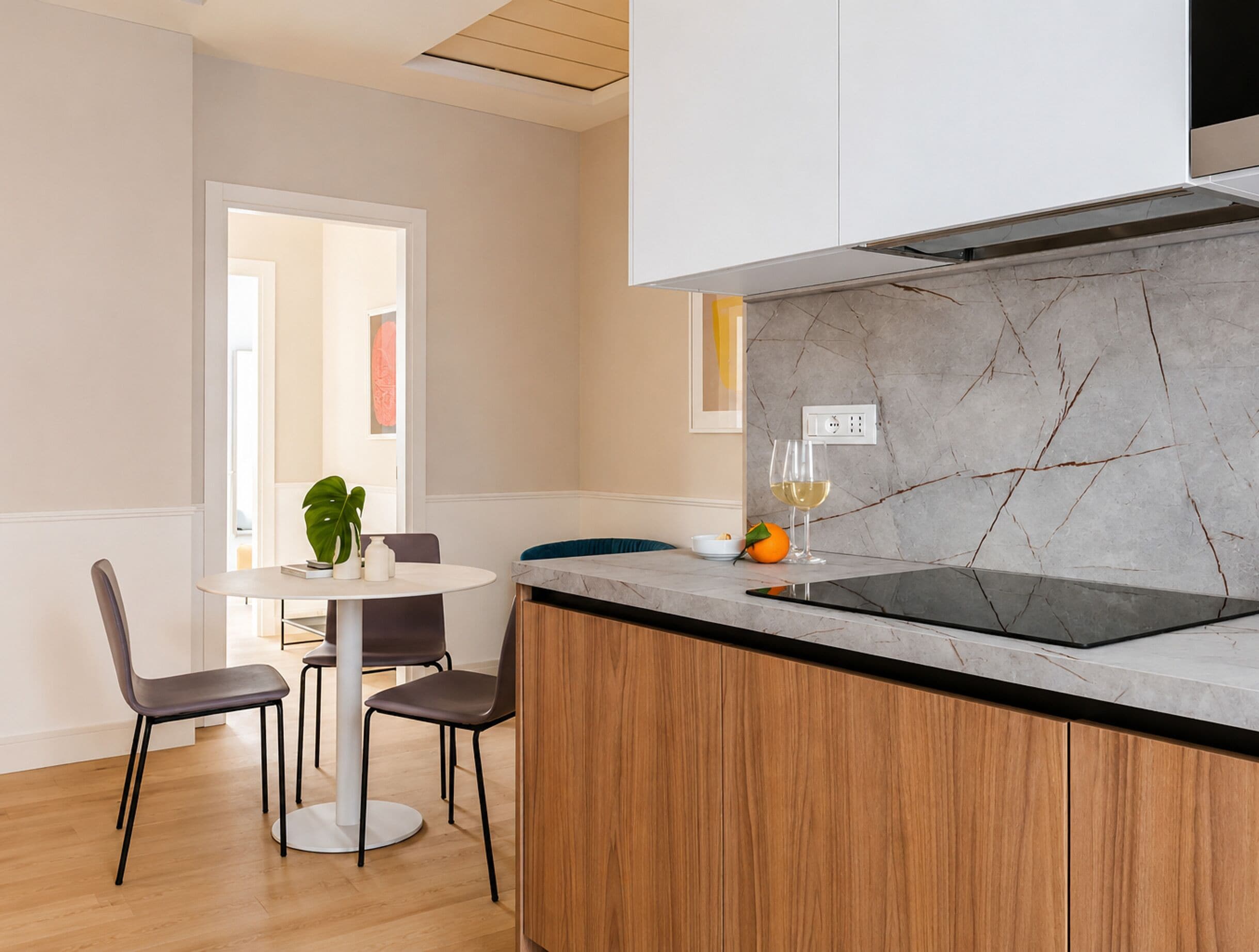 A modern kitchen with a marble backsplash, wooden cabinets, and a dining area with a round table and chairs.