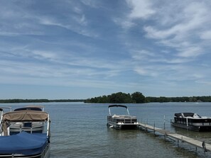 A lake with boats docked at a pier, a small island in the distance, and a clear sky.