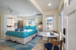 A bedroom with a bed, a desk, a chair, a small table, and a window. - Studio condo with AC in charming Oceanside (Oceanside)