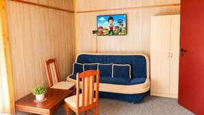 Une pièce de taille modeste, avec un canapé bleu, une table à manger en bois entourée de chaises, une petite plante en pot et une porte rouge.
