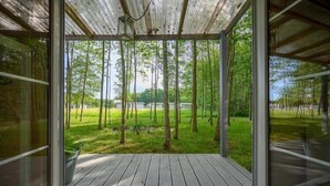 Una habitación con un amplio ventanal, una terraza de madera y vistas a un espacio verde con árboles.
