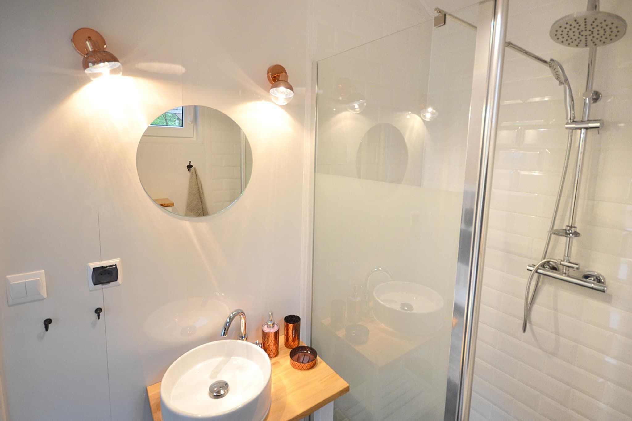 Une salle de bain moderne avec une douche à parois de verre, un miroir rond et un plan de toilette en bois avec un lavabo.