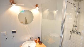 Une salle de bain moderne avec une douche à parois de verre, un miroir rond et un plan de toilette en bois avec un lavabo.